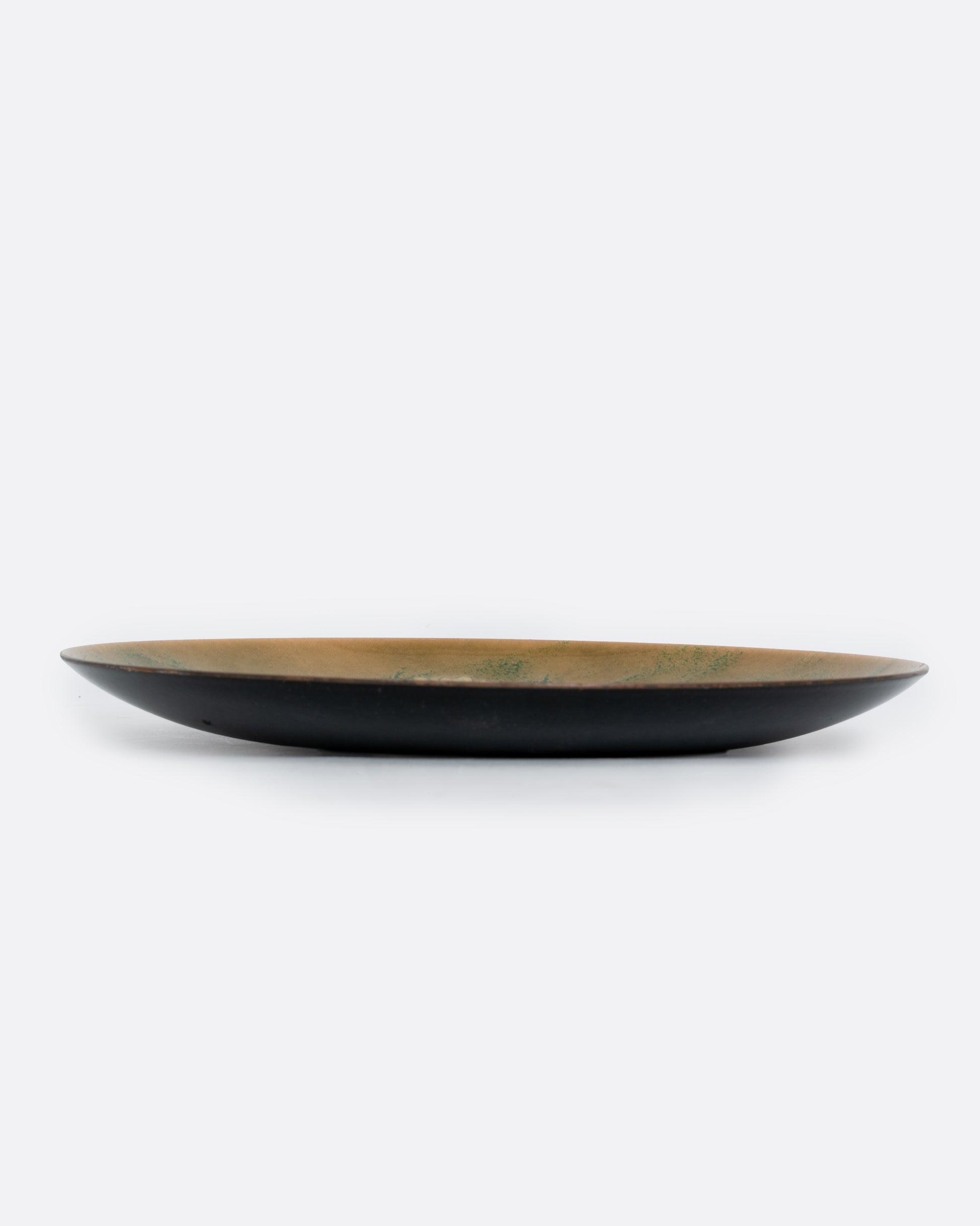 A metal and enamel plate with an abstract cluster design in green and yellow. Shown from the side.