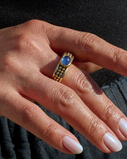 A yellow gold ring with a sapphire and dotted pattern on the band, shown worn on a hand.