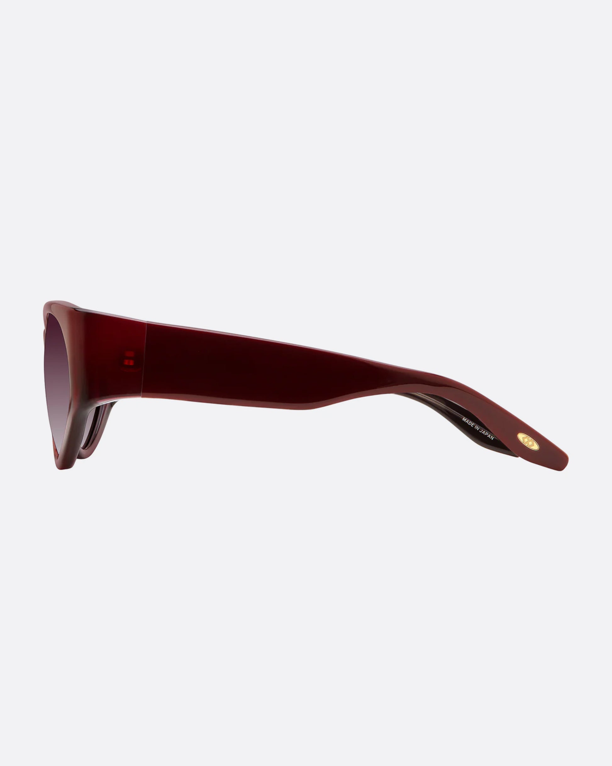 A pair of burgundy sunglasses with gradient lenses. Shown from the side.