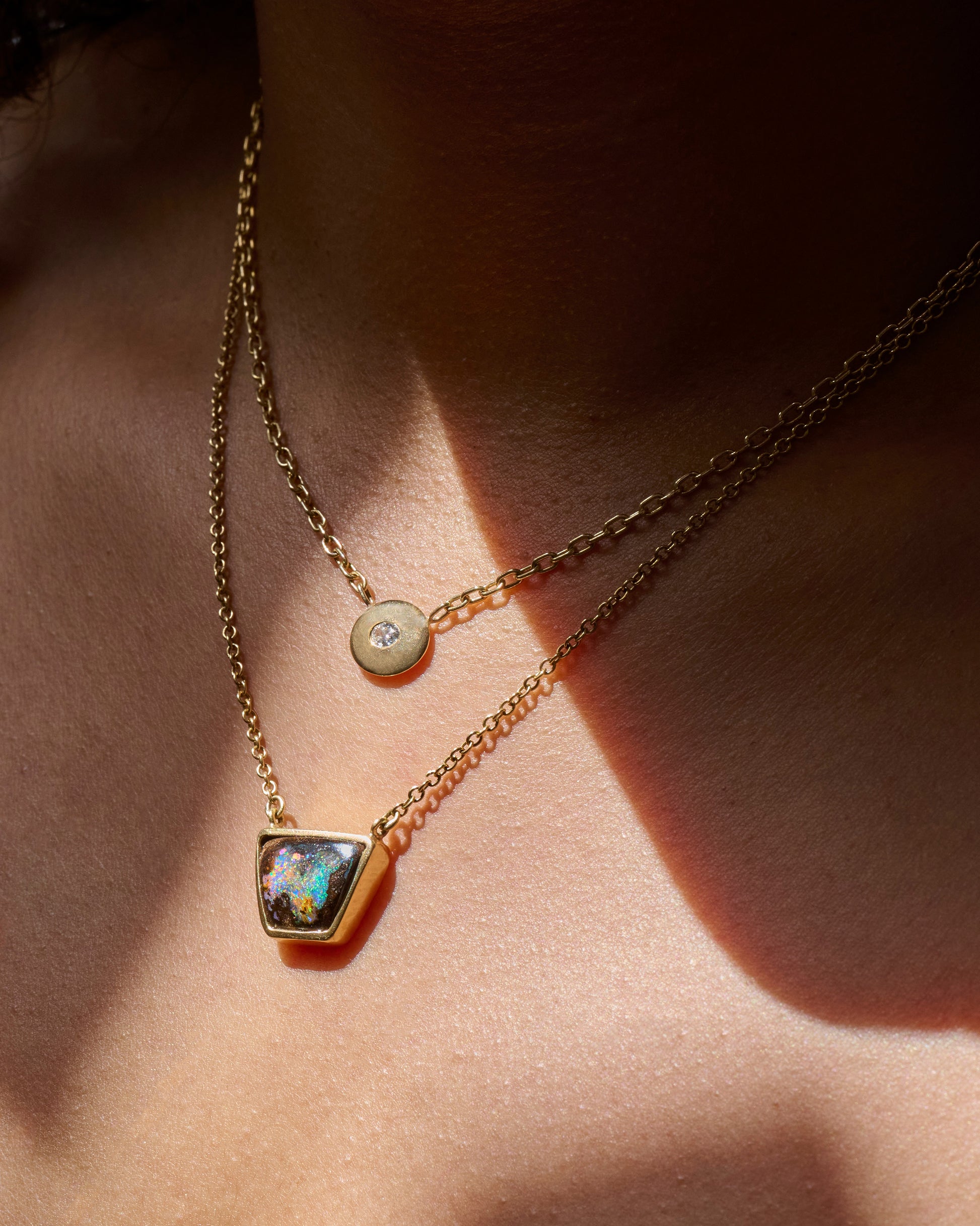 A yellow gold cable chain necklace with a trapezoidal opal set in a bezel. Shown from the side on a person.