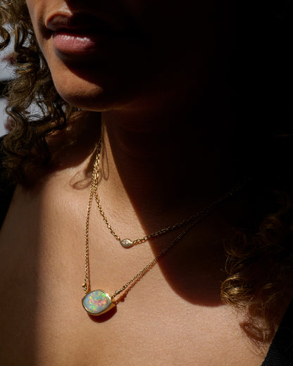 A yellow gold cable chain necklace with a large eye shaped opal pendant and diamond accents. Shown worn around the neck.
