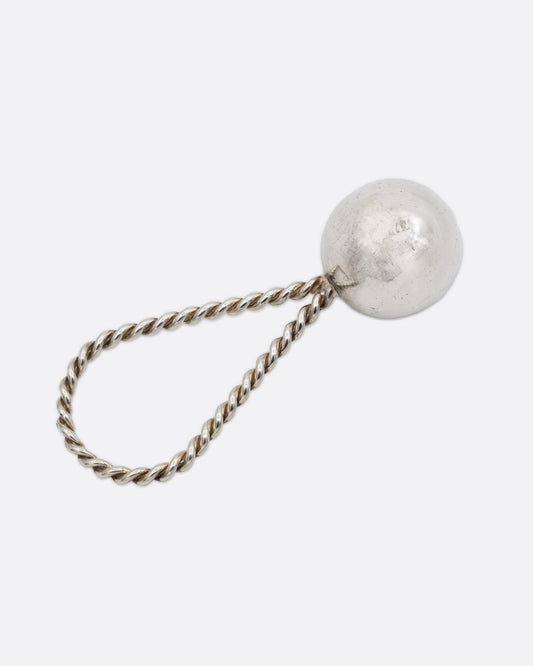 A silver rattle with a sphere at one and a twisted loop at the other. Shown from the back.