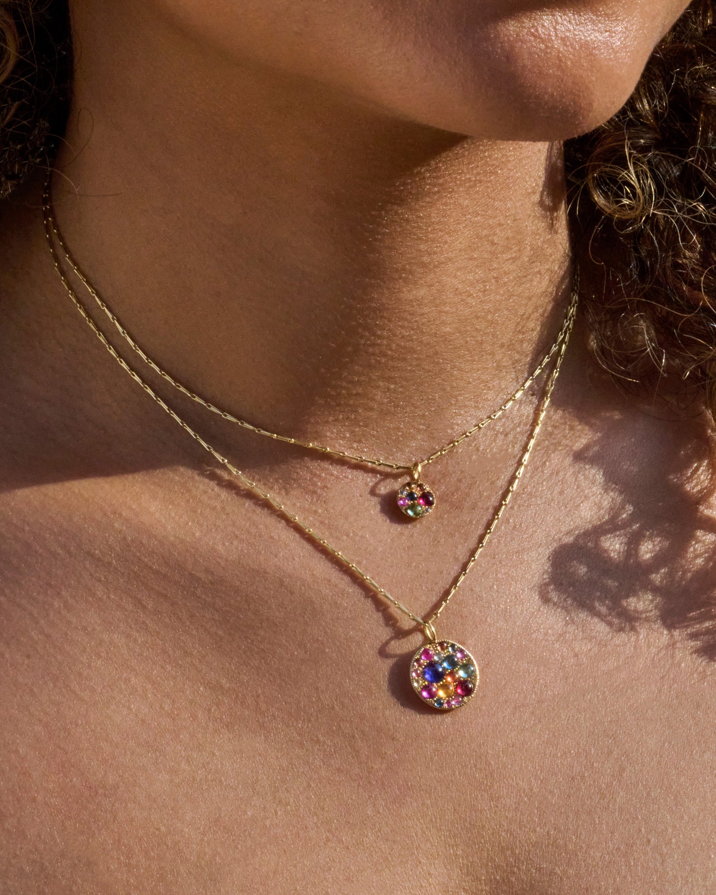 A yellow gold pendant with multicolor cabochon sapphires. Show worn on a chain.