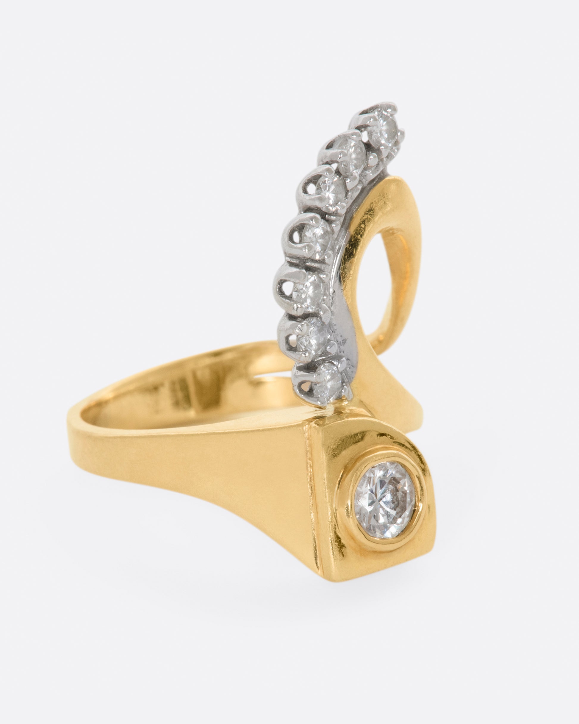 Yellow gold abstract ring with one bezel set round diamond and seven prong set diamonds. View from the right side.