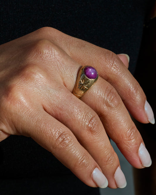 A domed yellow gold vintage ring with a ruby cabochon and starflower details. Shown worn on a finger.