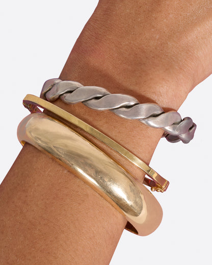 Vintage yellow gold cuff bracelet worn on a wrist stacked with a twisted silver bracelet and a slim gold bangle