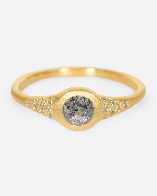 A brushed gold signet style ring with a salt and pepper diamond at its center and white diamond accents, shown from the front.