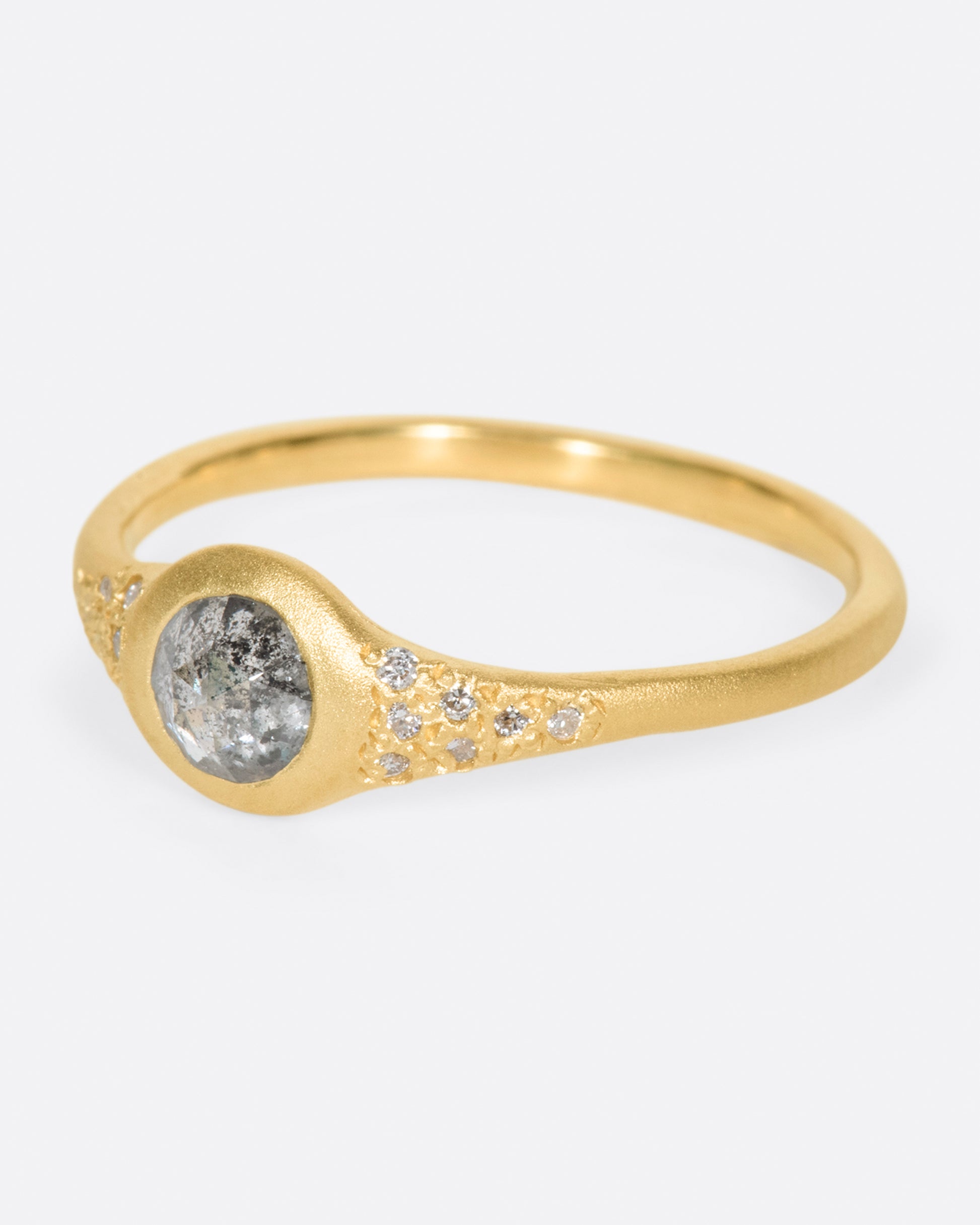 A brushed gold signet style ring with a salt and pepper diamond at its center and white diamond accents, shown from the side.