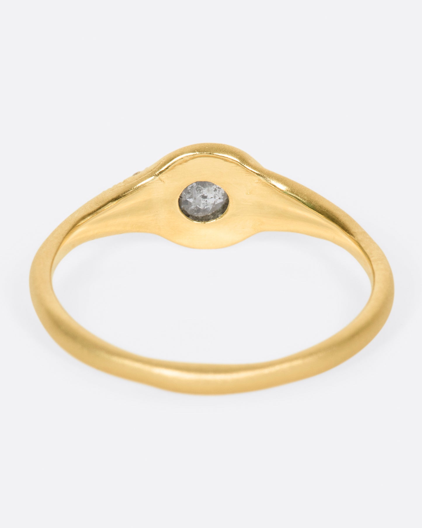 A brushed gold signet style ring with a salt and pepper diamond at its center and white diamond accents, shown from the back.