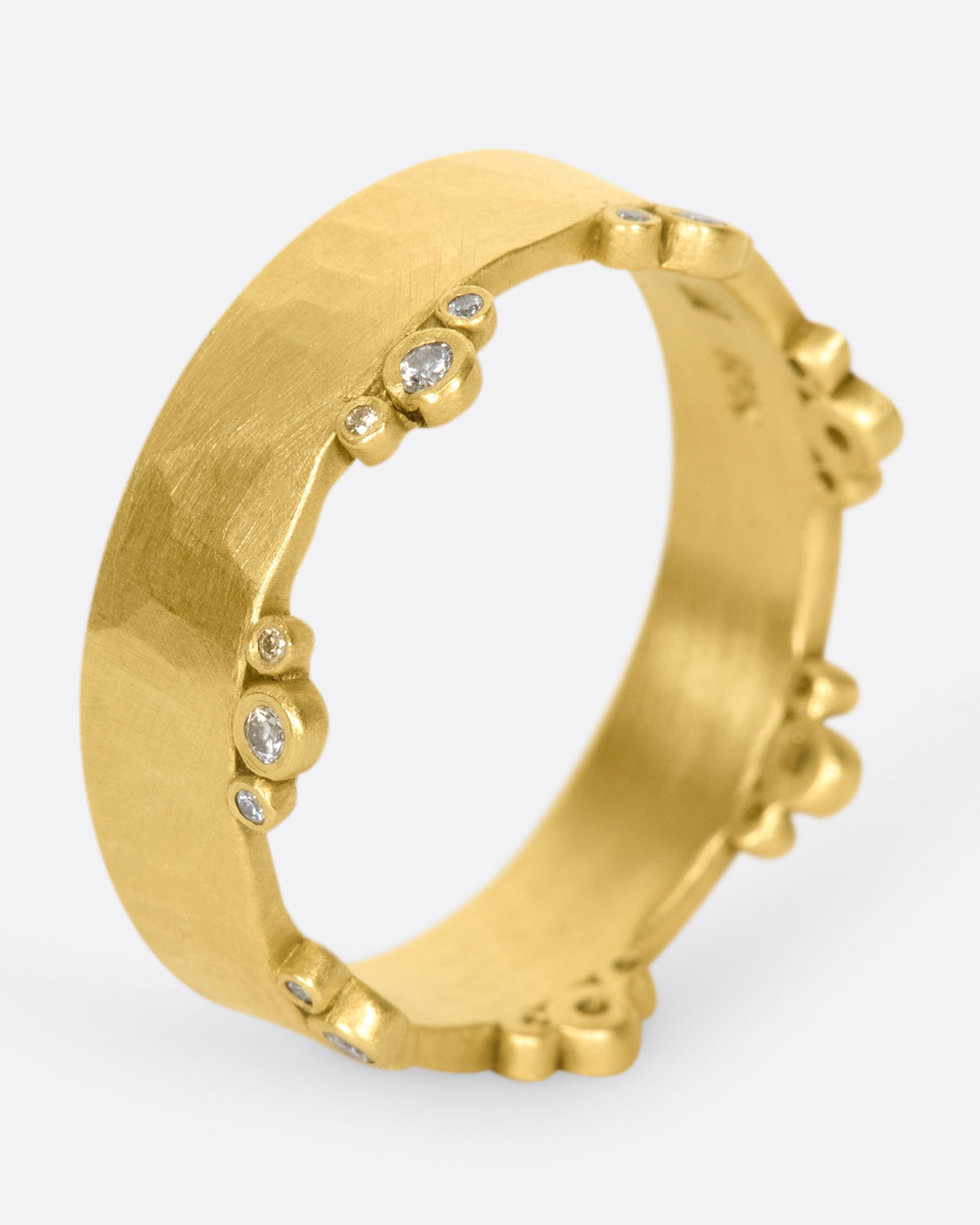 A wide, hammered, matte gold band with stations of diamonds along one edge.