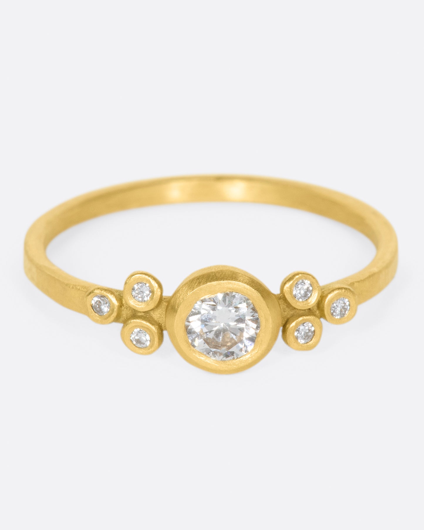 A hammered gold band with a round bezel set diamond at its center, flanked by three smaller round diamonds on either side.