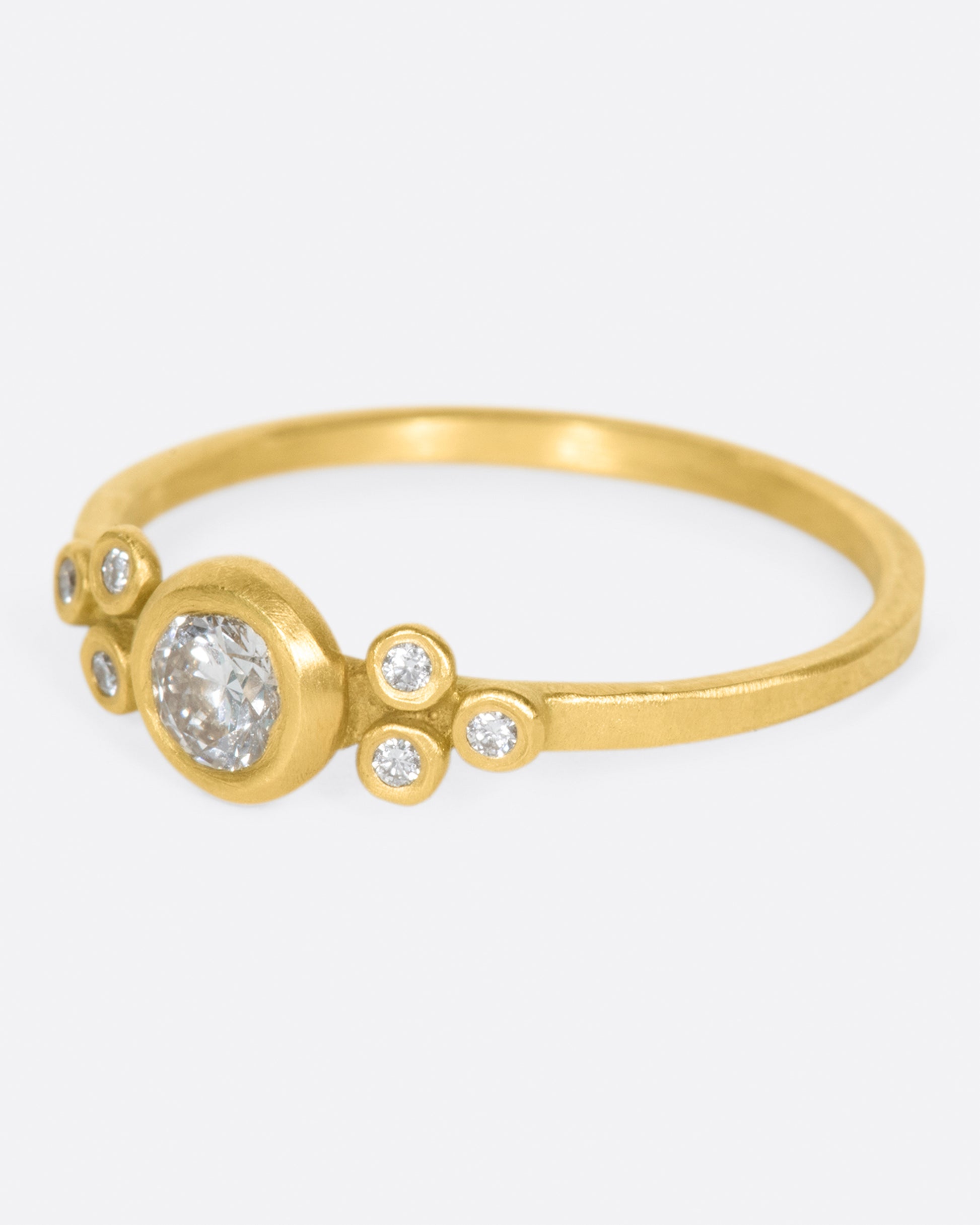 A hammered gold band with a round bezel set diamond at its center, flanked by three smaller round diamonds on either side.