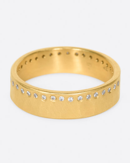 A hammered, matte gold band with a line of round diamonds all the way around. Shown from the front.