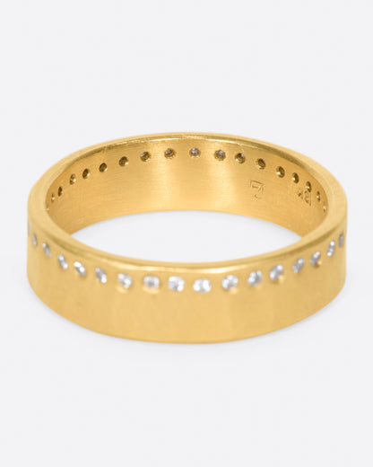A hammered, matte gold band with a line of round diamonds all the way around. Shown from the front.