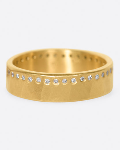 A hammered, matte gold band with a line of round diamonds all the way around. Shown from the front.