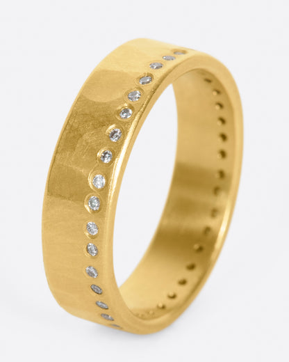 A hammered, matte gold band with a line of round diamonds all the way around. Shown standing up from the side.