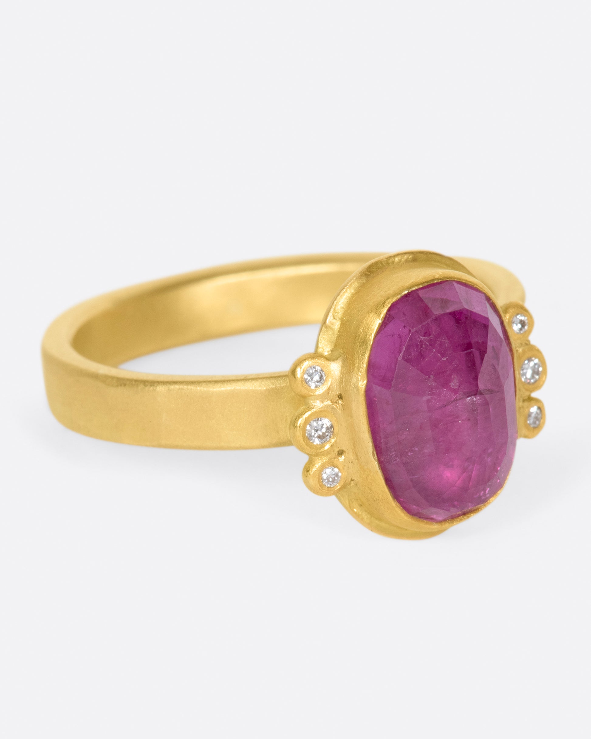 A saturated, faceted ruby shines in a high karat gold bezel with diamond accents.