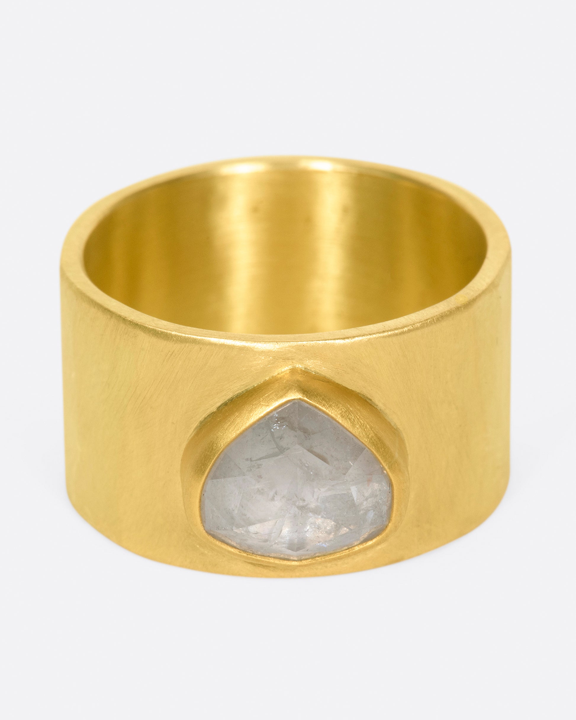 A wide, matte, hammered band with a rose cut gray diamond embedded in a high karat gold setting.