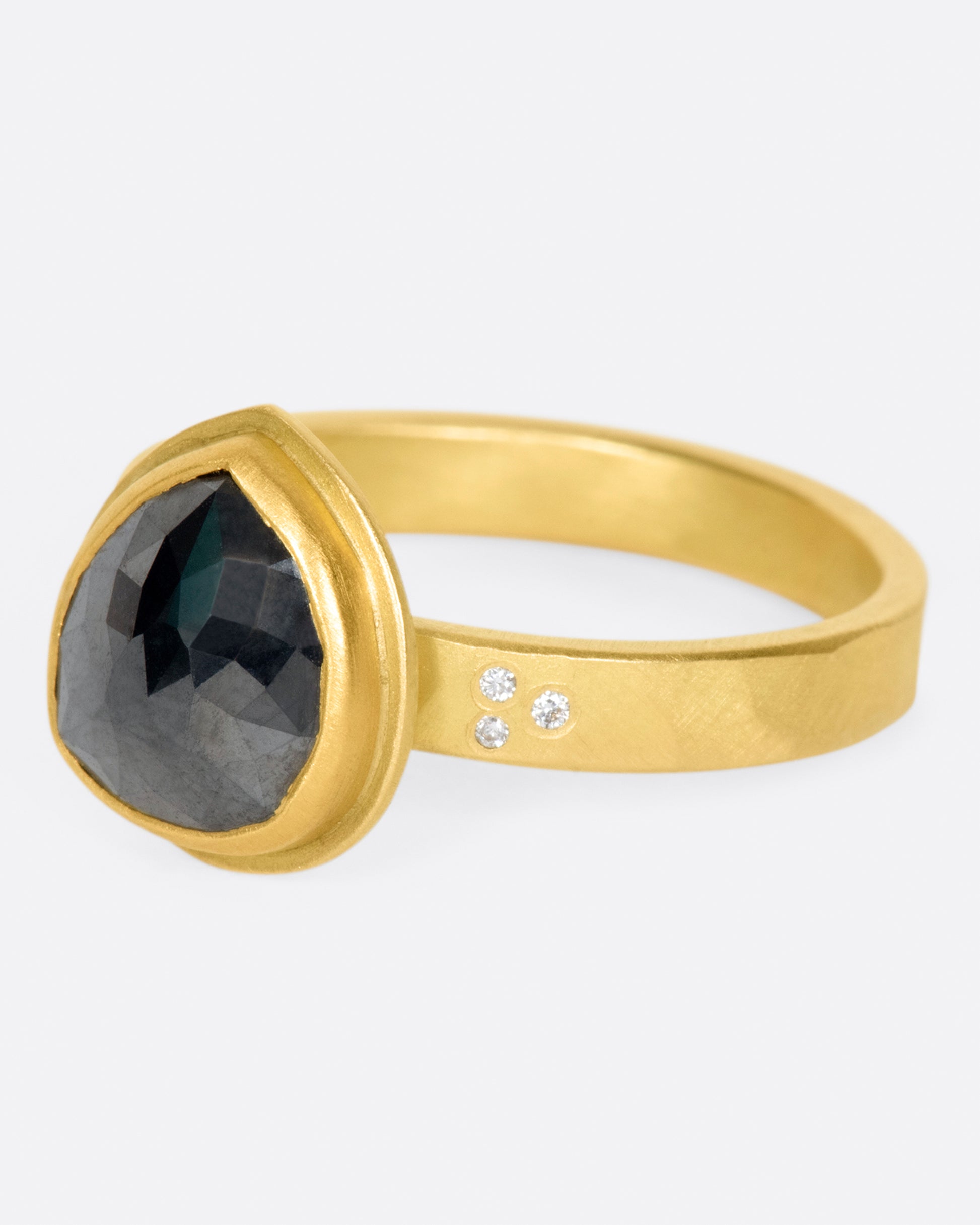 A faceted, pear shaped black diamond in a 22k gold setting with white diamond accents.