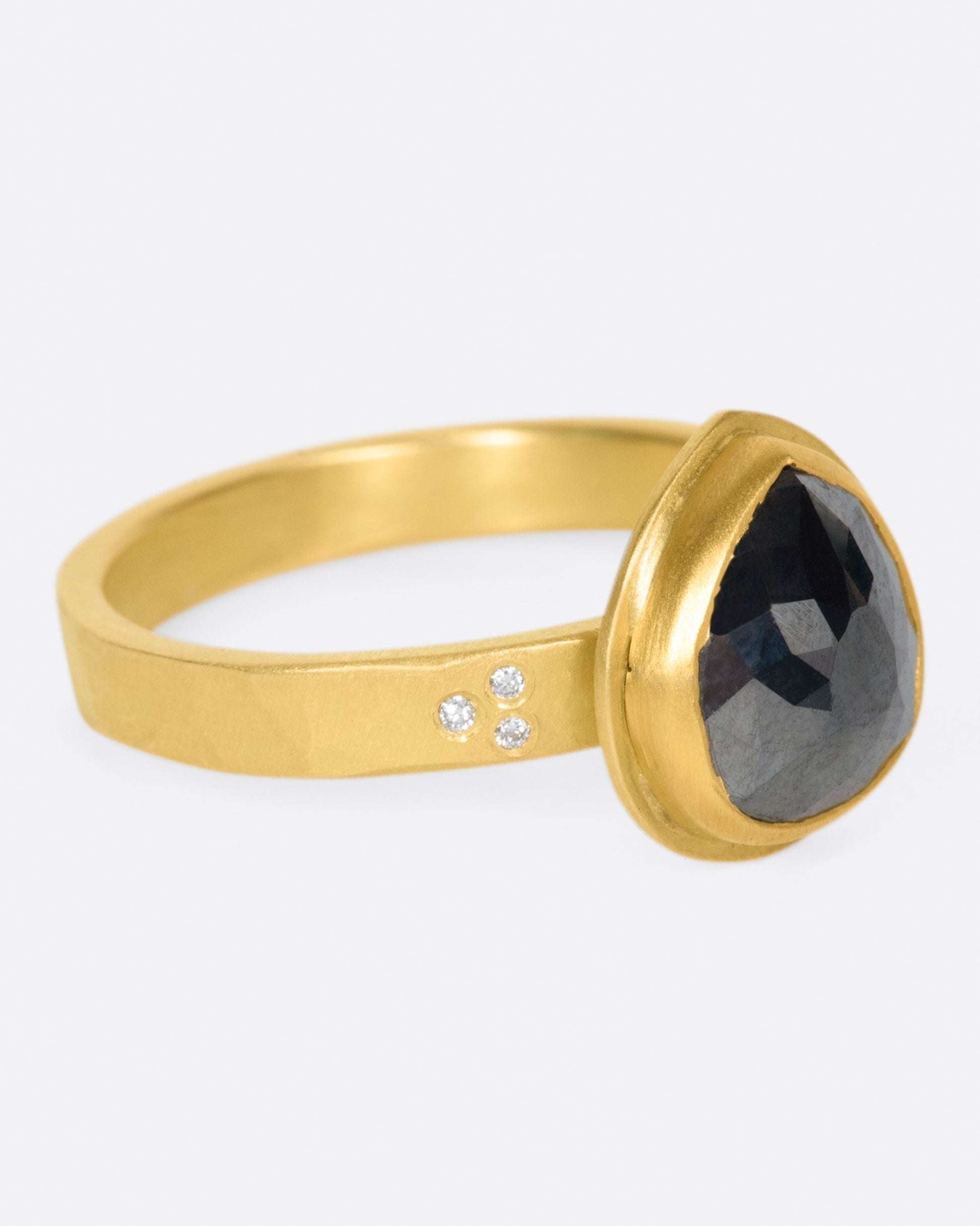 A faceted, pear shaped black diamond in a 22k gold setting with white diamond accents.