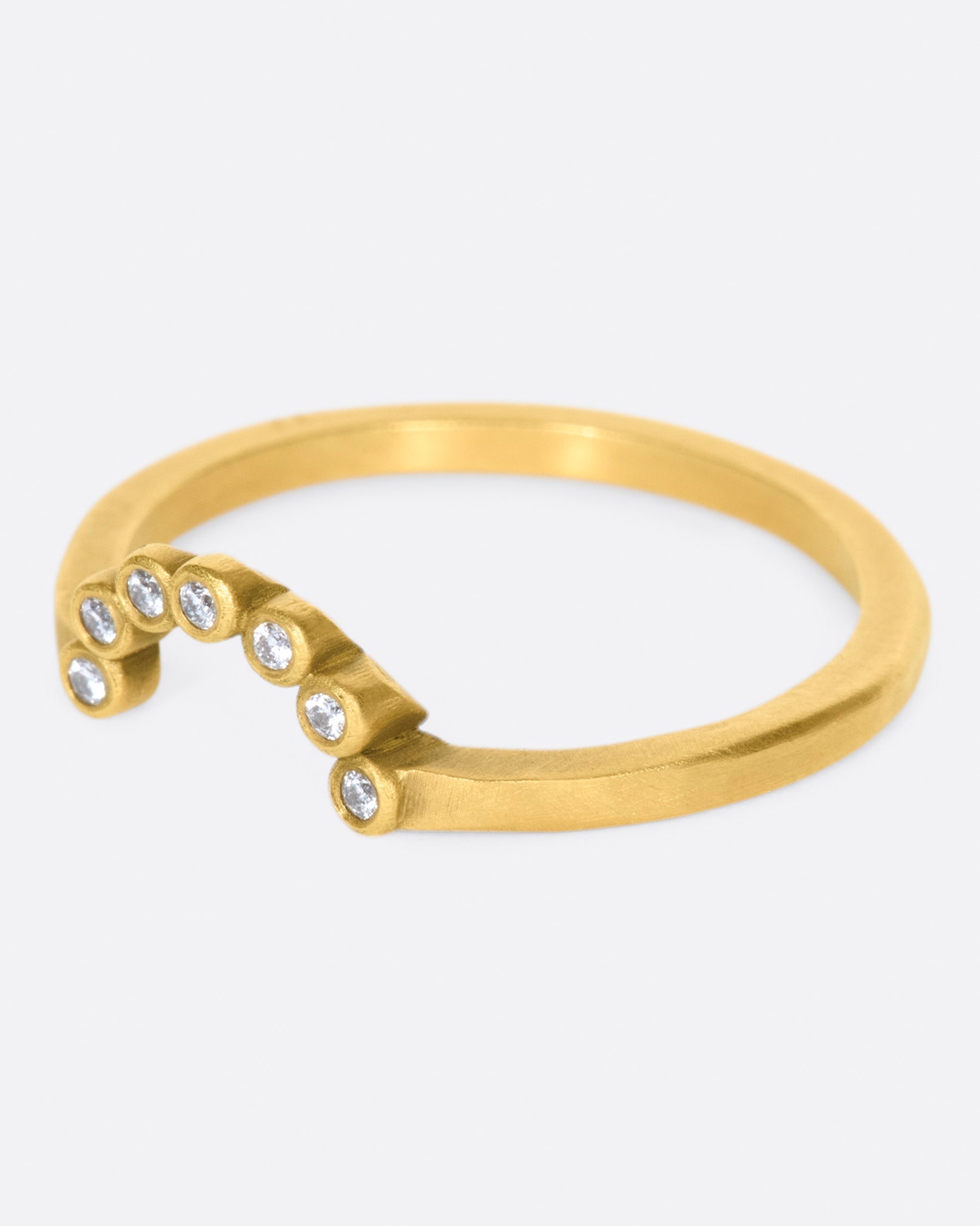 A matte gold ring with an arc of seven bezel set diamonds.