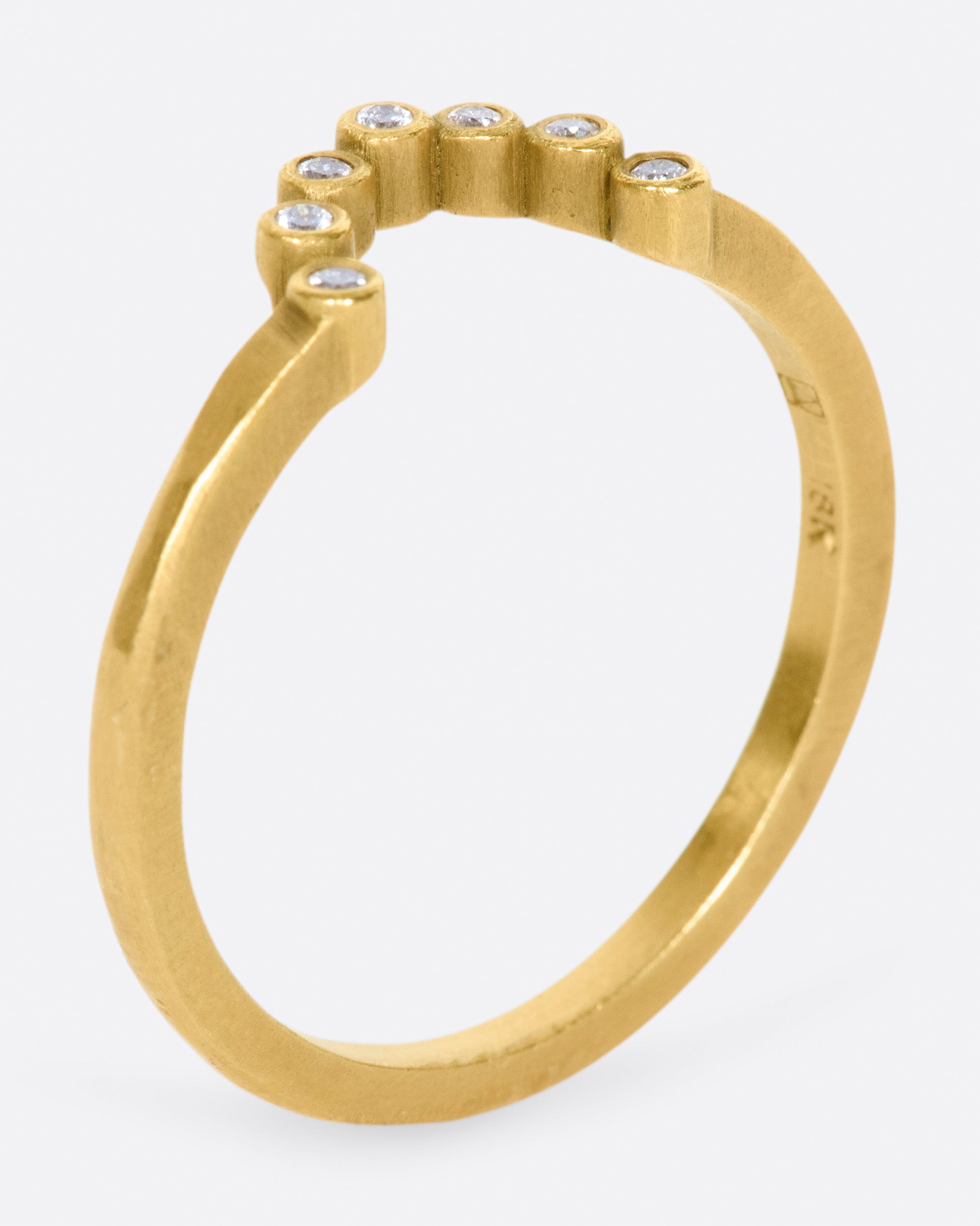A matte gold ring with an arc of seven bezel set diamonds.