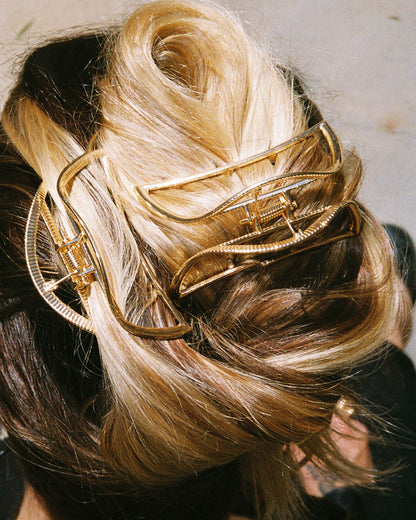 A woman's blond hair twisted up in two gold hair clips with spring loaded tops and teeth at the bases. Shown from the top.