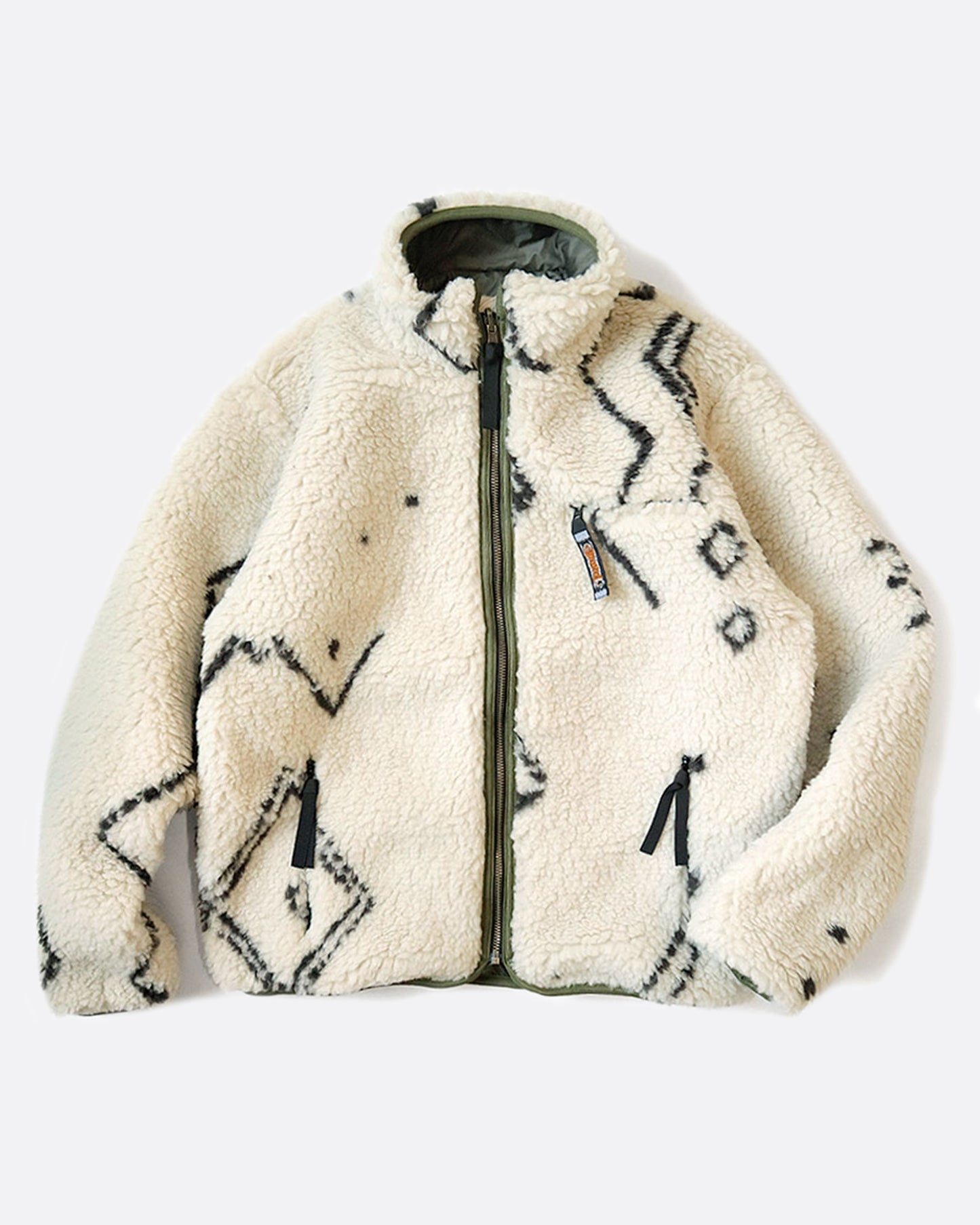 A reverisble jacket with white Beni Ourain patterned fleece on one side and a green nylon shell on the other, shown laying flat on the fleece side.