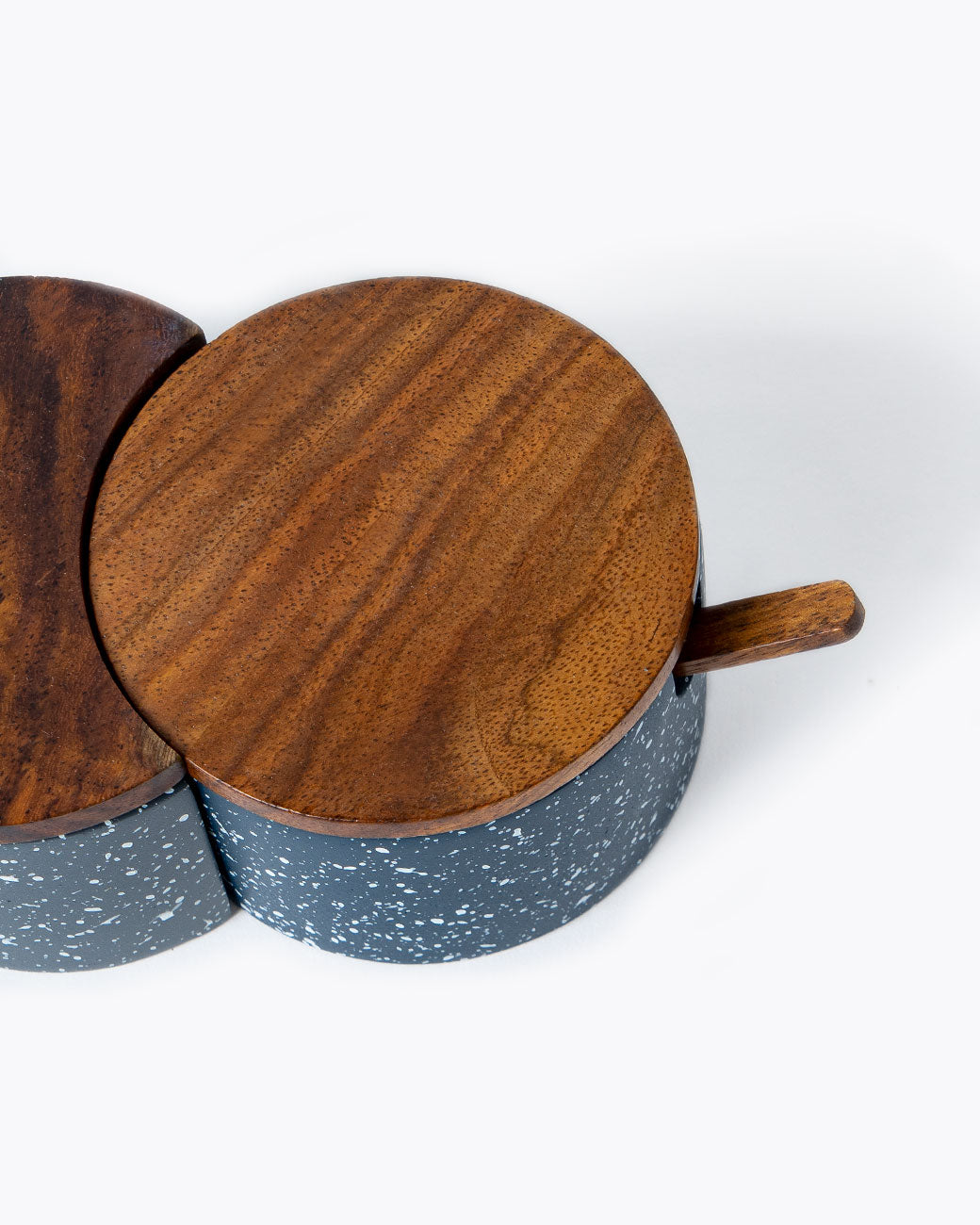 Interlocking circular salt cellar made of speckled blue and gray cement with wood lid and spoon, shown from the top.