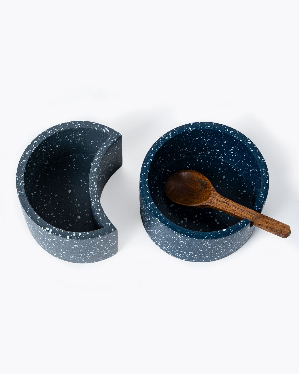Interlocking circular salt cellar made of speckled blue and gray cement with wood lid and spoon, shown from the top without the lids.