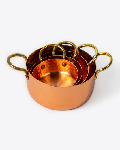 A set of four hammered copper measuring cups, stacked together. Shown from the front.