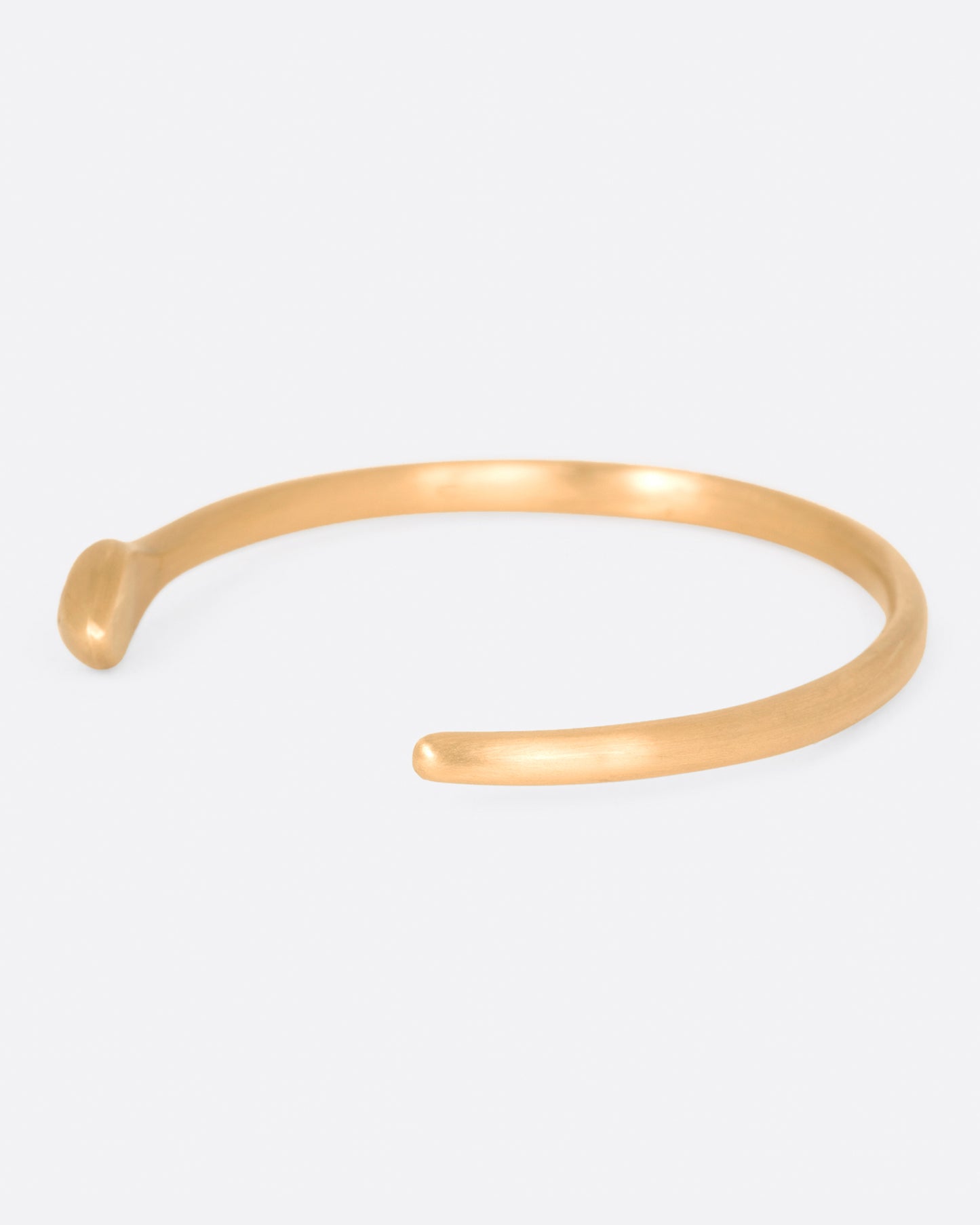 A matte yellow gold snake cuff bracelet with a pear shaped pink sapphire on its head, shown from the side.