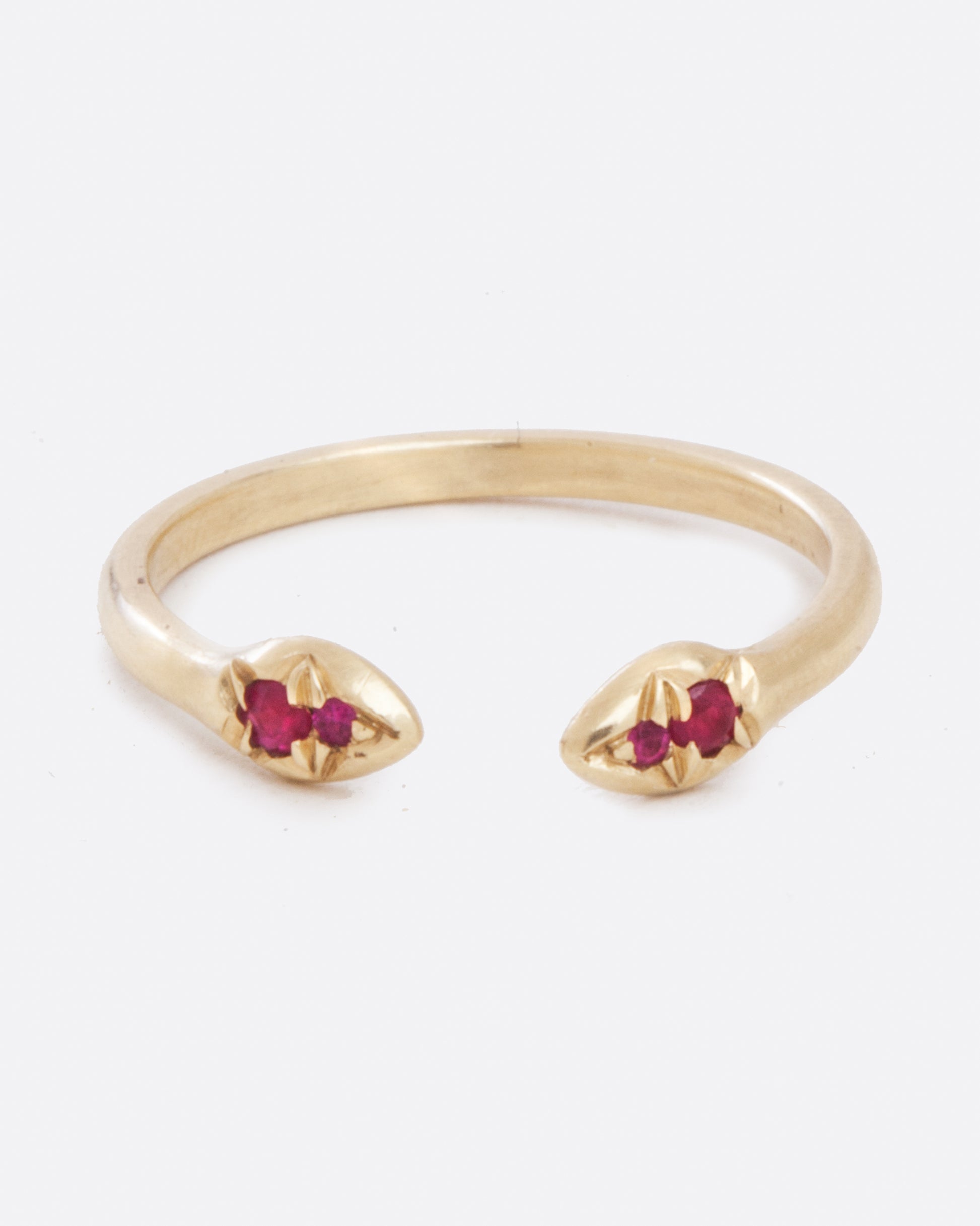 an open yellow gold ring from the front. the ends of the opening each have two red rubies set into it and is slightly bulbous.