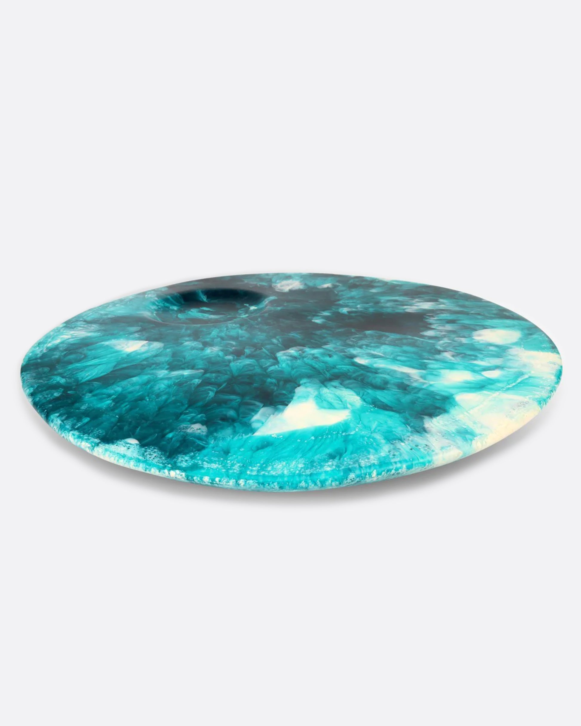 A round teal blue and white resin platter with a round indentation, shown from the side.
