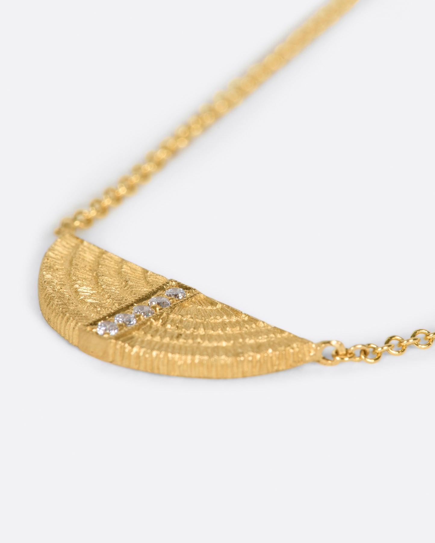 A necklace with a semi-circular pendant with five diamonds, shown laying flat.