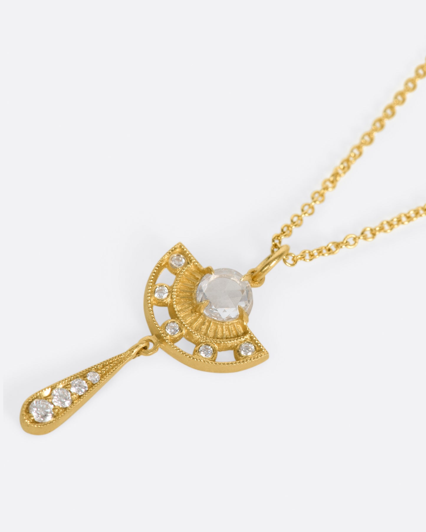 A semi circular pendant necklace with a rose cut diamond at its center and a second diamond drop, shown laying flat.