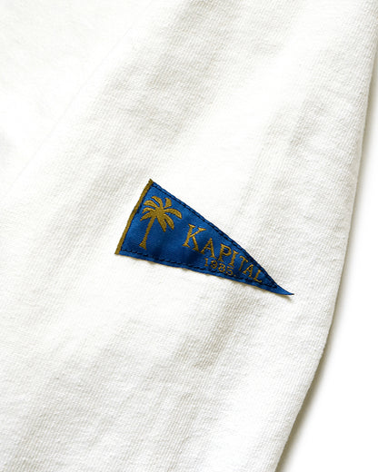 A close up of the blue pennant shaped tag on a white long sleeve shirt with hidden yellow smileys peeking out at the elbows. 