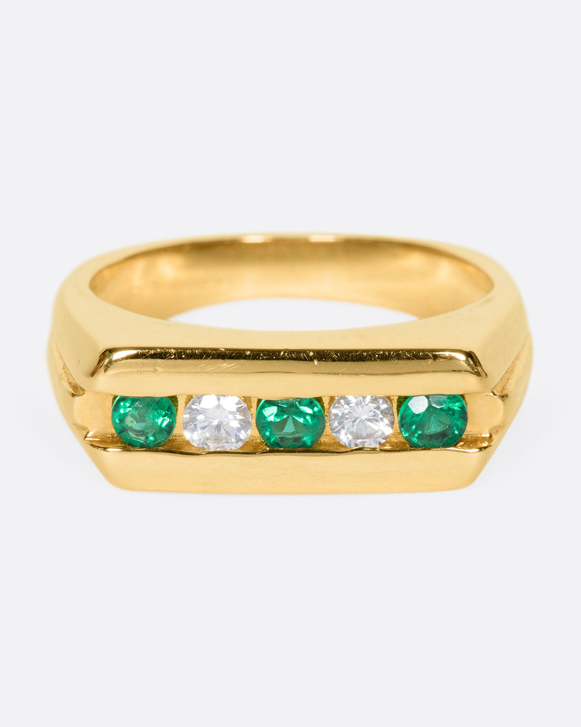 The face of this ring features five channel set stones; three emeralds and two diamonds.