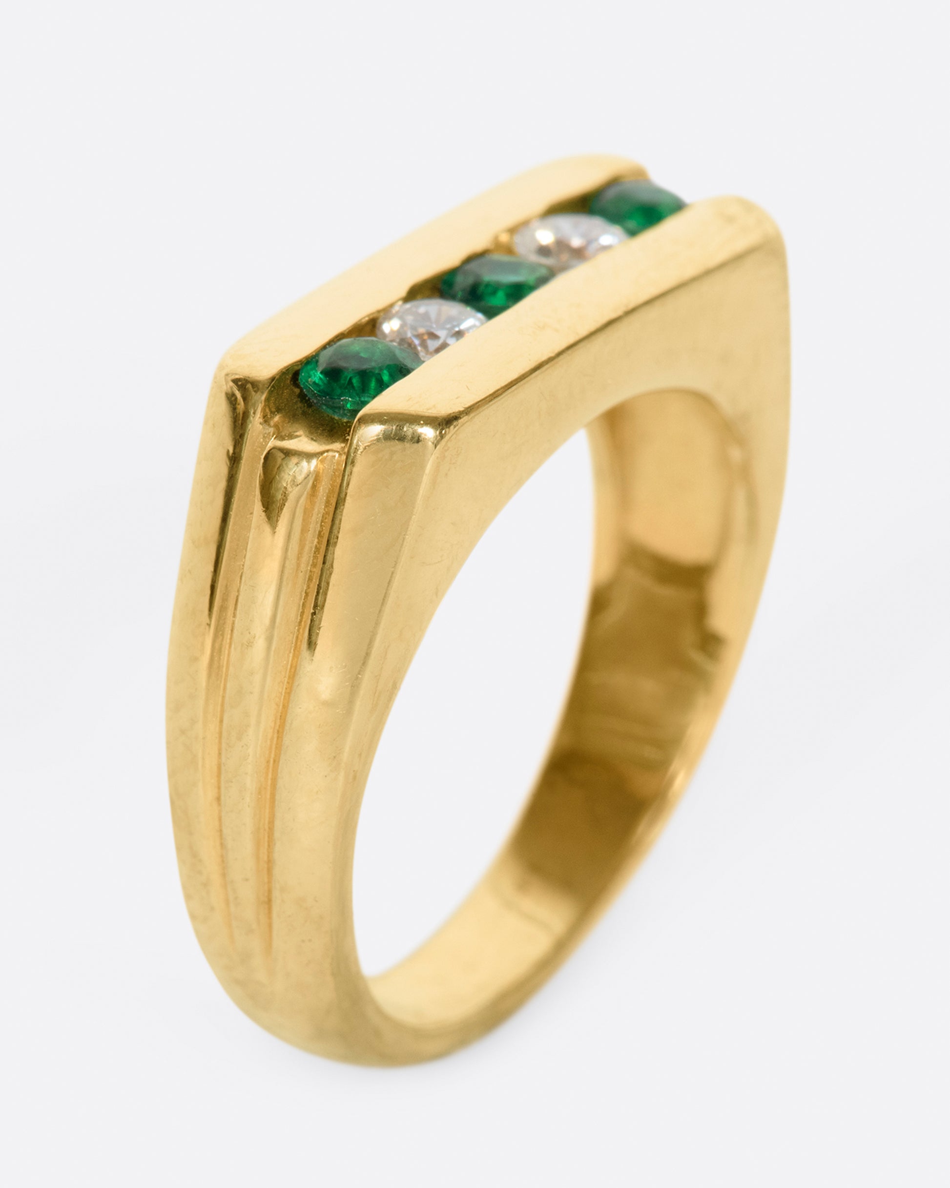 The face of this ring features five channel set stones; three emeralds and two diamonds.