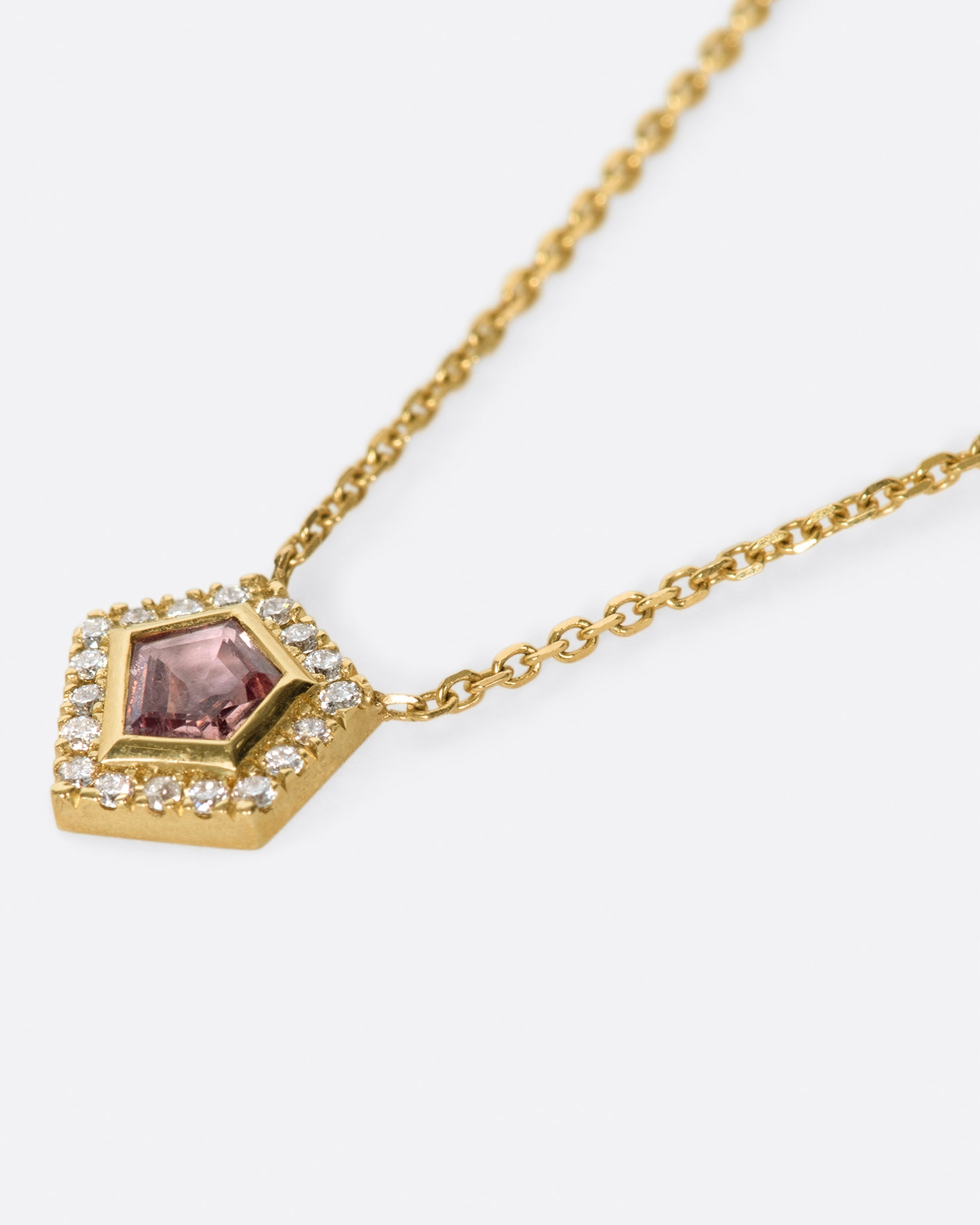 A shield shaped pink sapphire pendant necklace with a diamond halo, shown from the side.