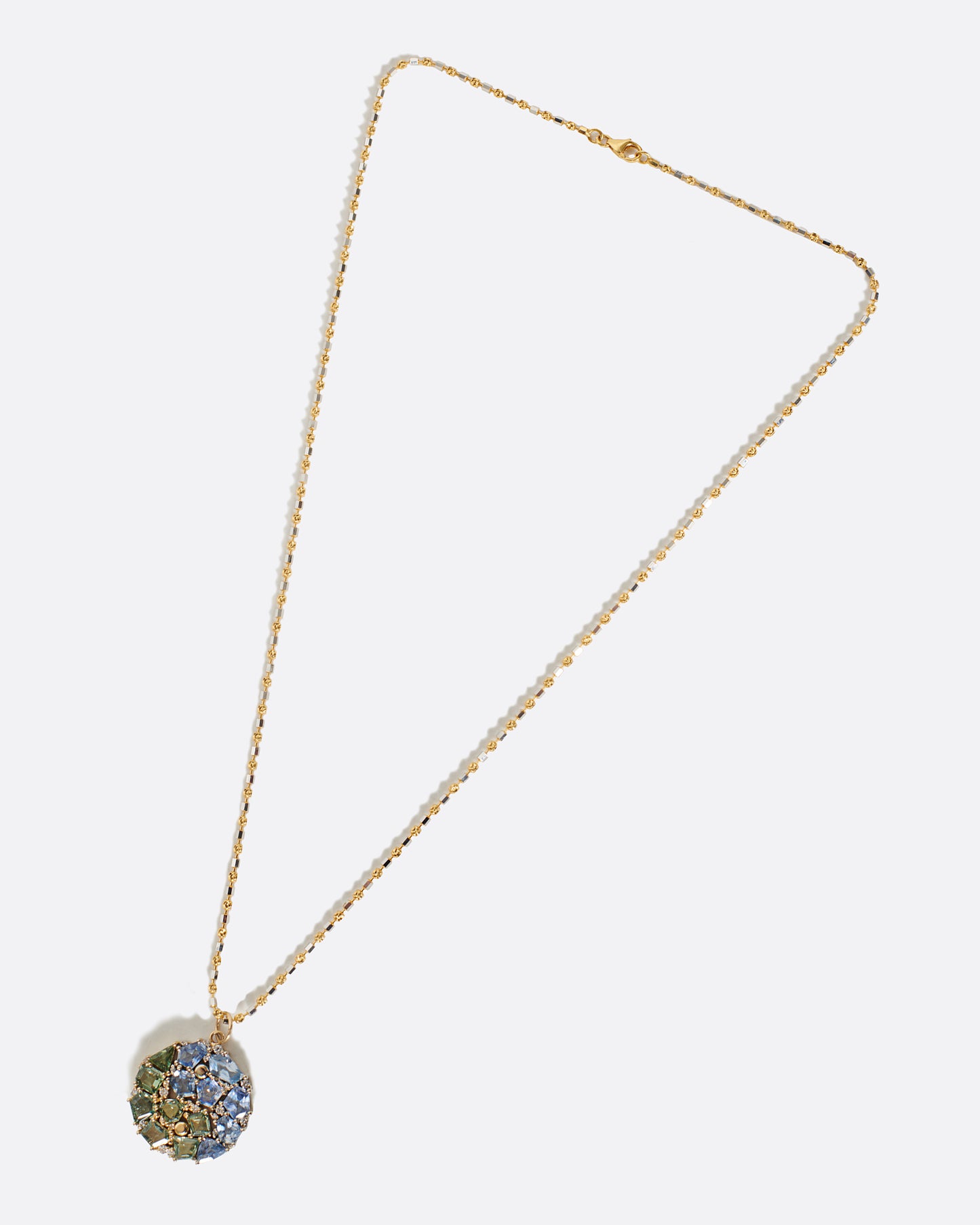 A two-tone yellow and white gold chain with a mosaic blue and green sapphire yin yang pendant.