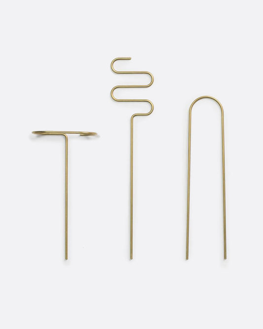 three brass plant sticks side by side on a white background, each one is bent into a different shape