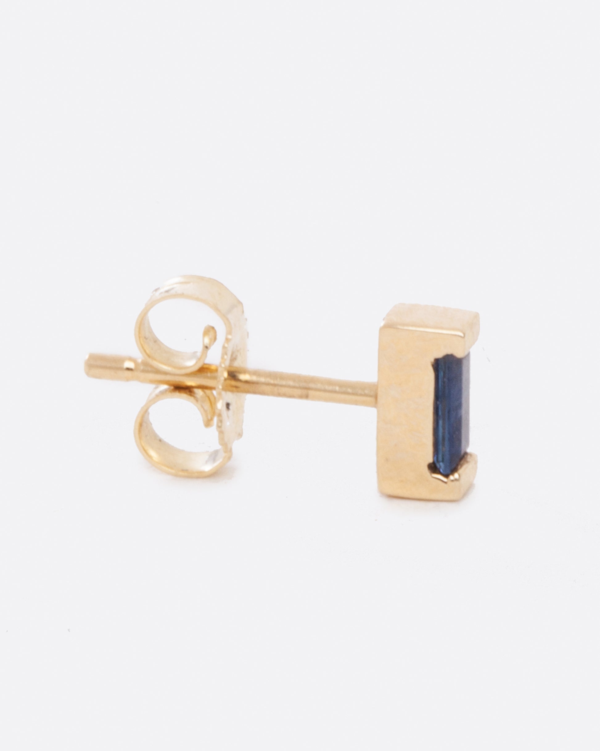 a small yellow gold single earring with a small blue sapphire baguette, shot from the side with the straight back and butterfly backing visible