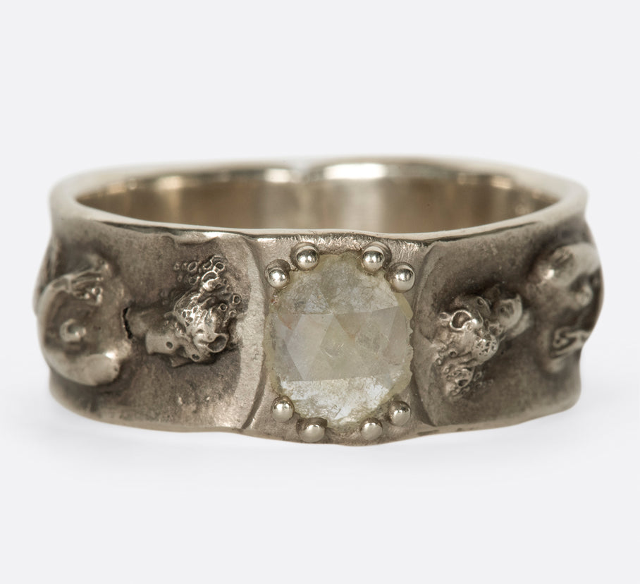A white gold band with a rose cut diamond at its center and a female figure on either side, shown from the front.