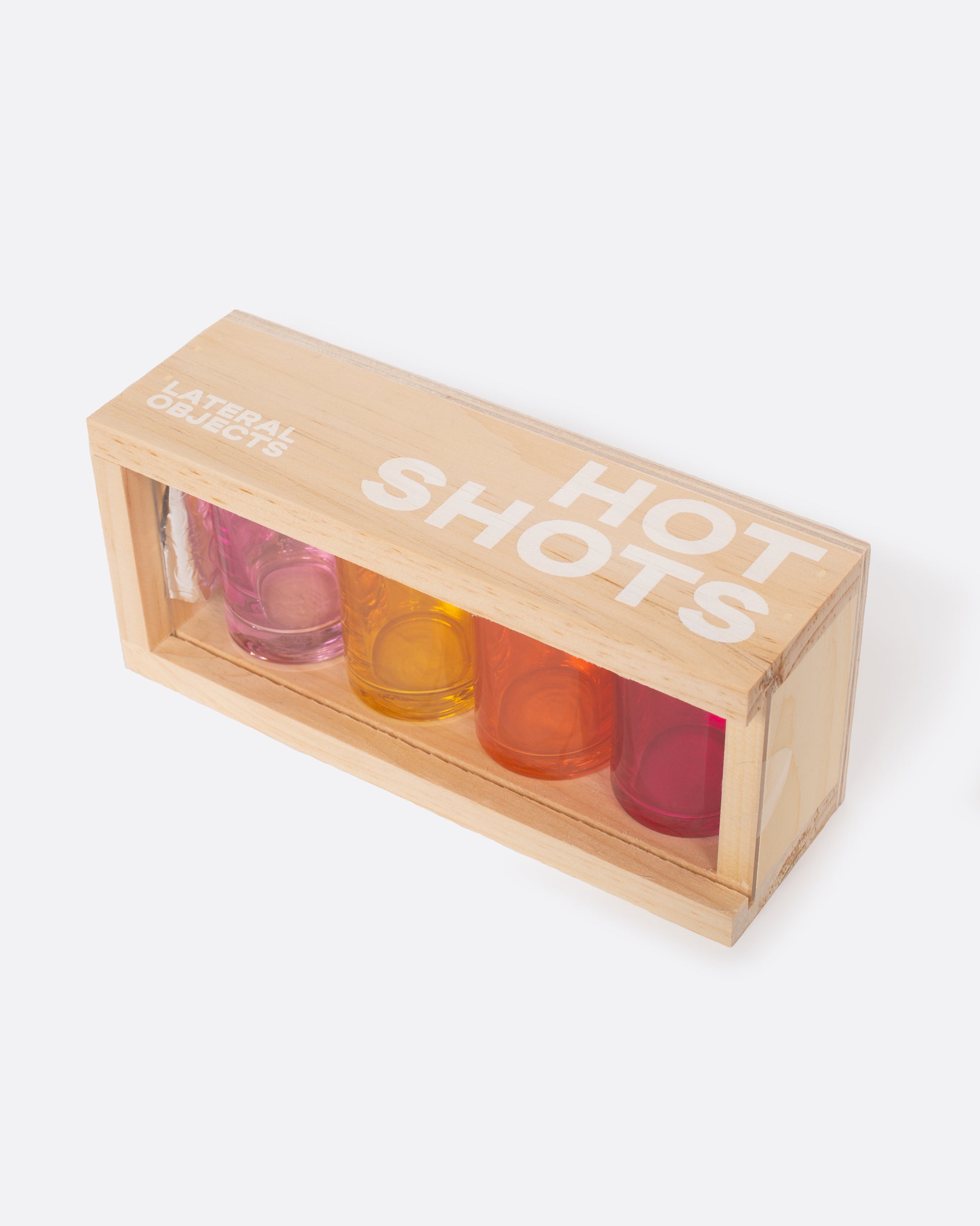 Four glass shot glasses in shades of pink, orange, and yellow, shown in their wood carrying case.