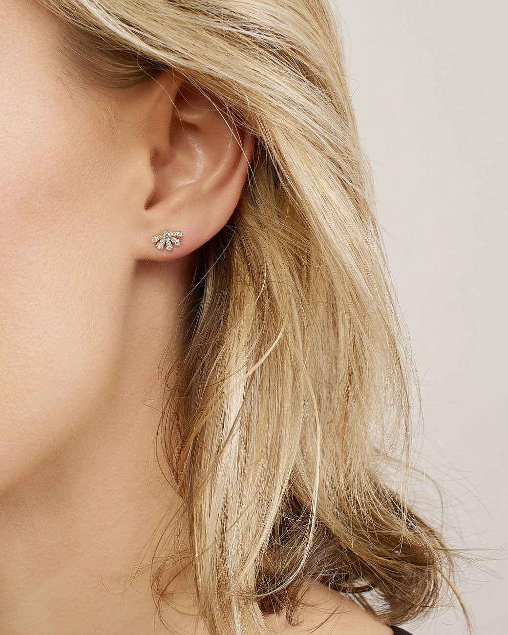 womans ear with a stud earring in it. it fits her lobe perfectly. the middle diamond has rays of more diamonds extending from it on one side.