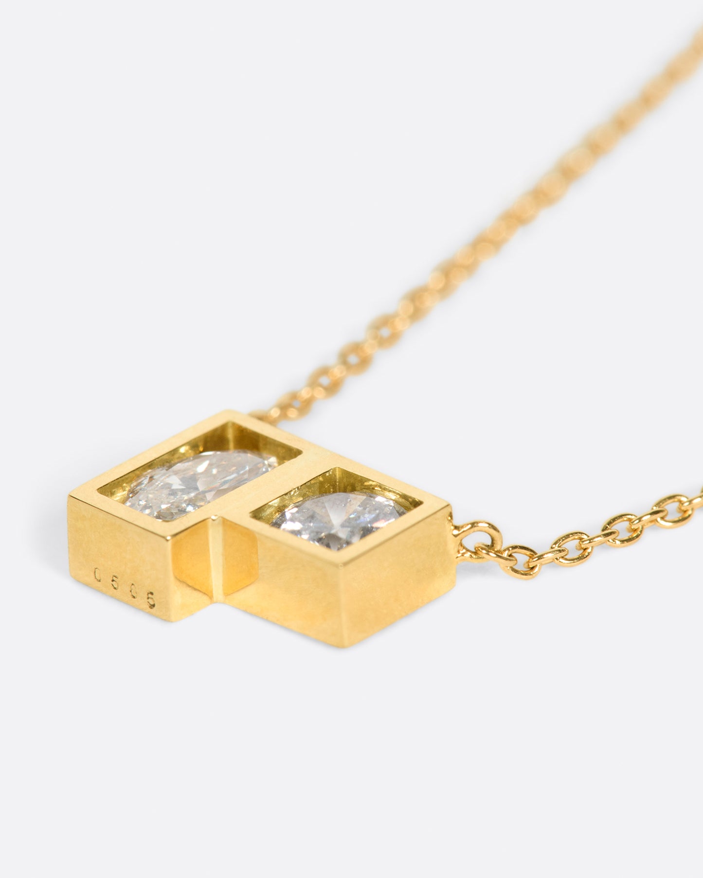 A geometric pendant necklace with two diamonds, shown laying flat.