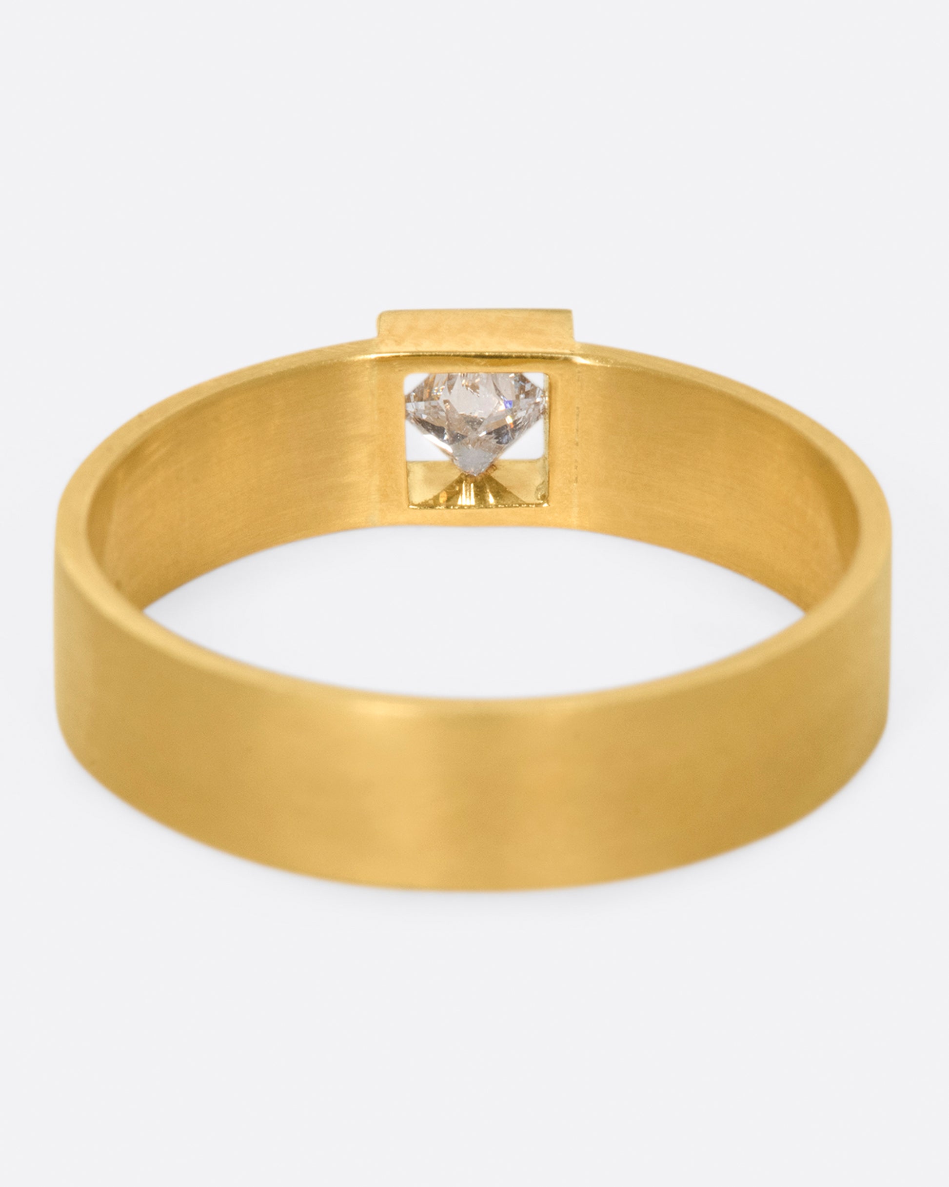 A wide, matte band ring with a princess cut diamond set at its center.