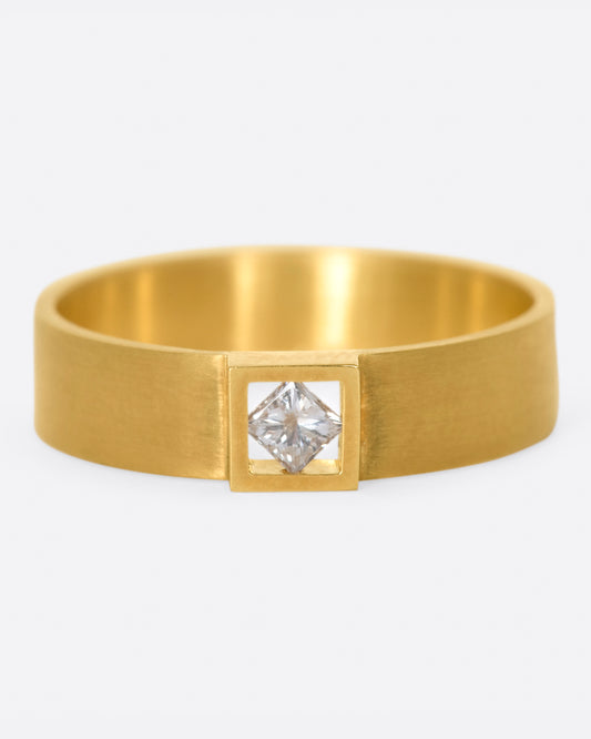 A wide, matte band ring with a princess cut diamond set at its center.