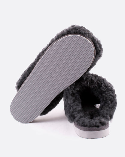 A pair of Jenny sheepskin slippers in charcoal gray. One slipper is shown from the bottom, the other is shown from the back.